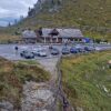 Mehrere Autos stehen im Vordergrund auf einem Parkplatz vor einer Berghütte auf der Tour Kurvenjagd
