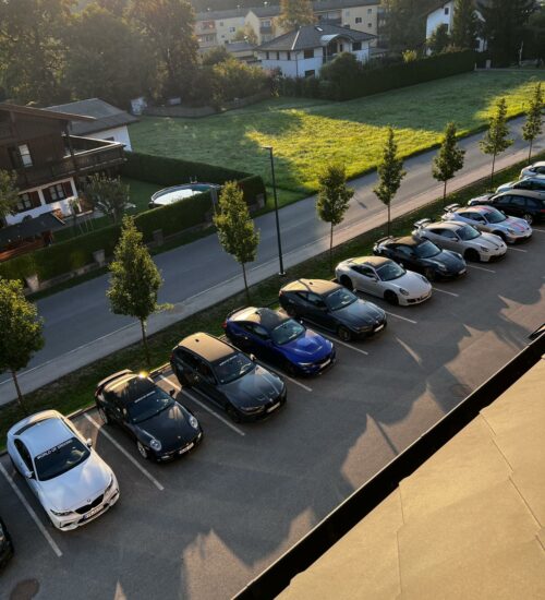 Mehrere Autos stehen auf einem Parkplatz vor einem Hotel auf der Tour Kurvenjagd